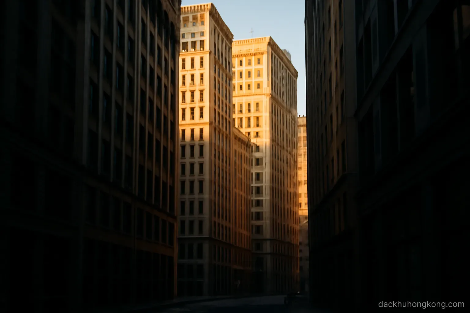 late afternoon sun striking the upper floors of closely packed towers while the street below stays in deep shadow