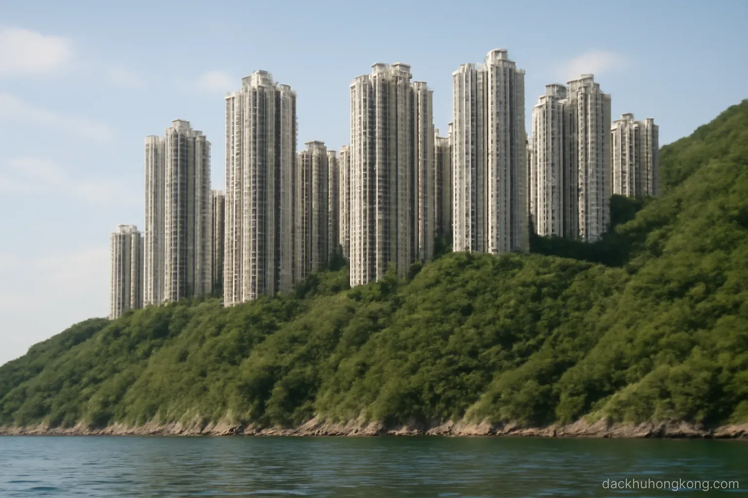 a wall of slender high rise towers rising directly from a steep green hillside above the water